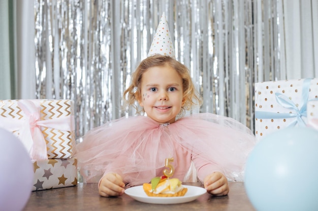 Фото Милая маленькая девочка с короткими вьющимися волосами и звездами на лице в розовом пышном платье и кепке выглядит улыбающейся