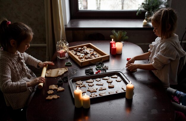 Cute little girls are cooking Christmas gingerbread on a wooden table Family pastime preparation for the Christmas holidays