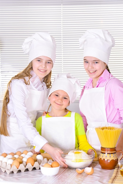 Cute little girls in chef's hats and aprons preparing dough in the kitchen at home