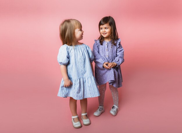 Cute little girls looking at camera and smiling isolated on pink background