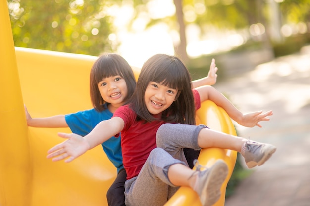 晴れた夏の日に屋外の遊び場で楽しんでいるかわいい女の子の兄弟。プラスチック製のスライド上の子供たち。子供のための楽しい活動。子供のためのアクティブなスポーツレジャー