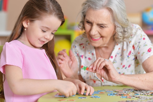 귀여운 작은 손녀와 할머니가 퍼즐을 모으는 중
