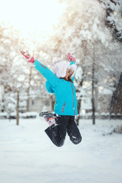 Cute little happy girl in winter clothes is having fun jumping in snowy winter day.