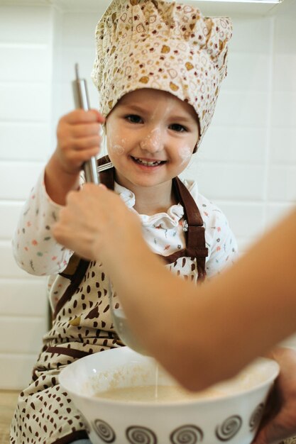 Cute little homecook girl with her beautiful mother makes pancakes in white kitchen