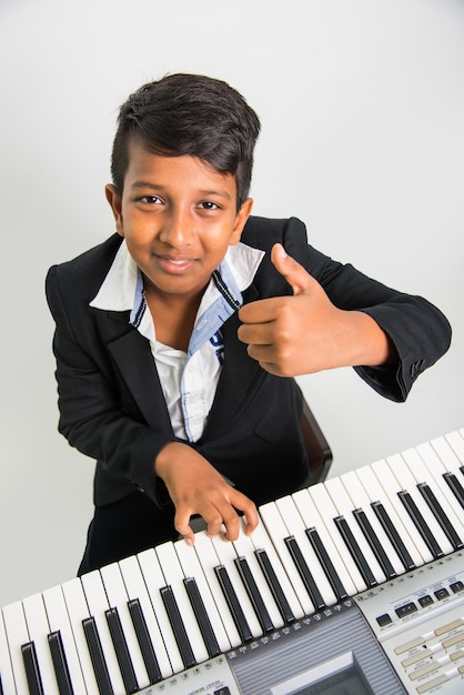 白い背景の上でピアノやキーボード、楽器を演奏するかわいい小さなインドやアジアの少年