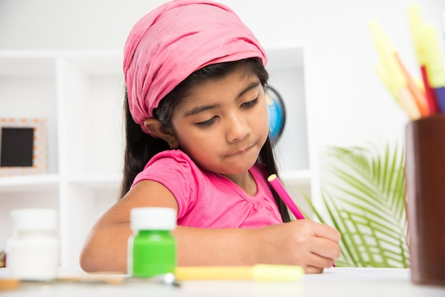 Симпатичная маленькая индийская или азиатская девочка, которая любит рисовать или рисовать кистью и раскрашивать бумагу дома