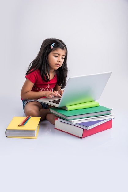귀여운 인도 또는 아시아 여자 아이 노트북에서 공부하거나 거짓말을하거나 바닥에 앉아있는 동안 학교 프로젝트에서 작업, 흰색 배경 위에 절연