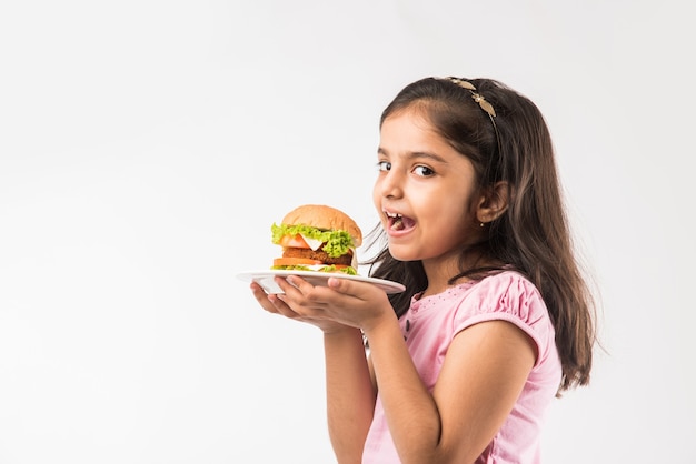 Cute little Indian or Asian girl eating burger on white background