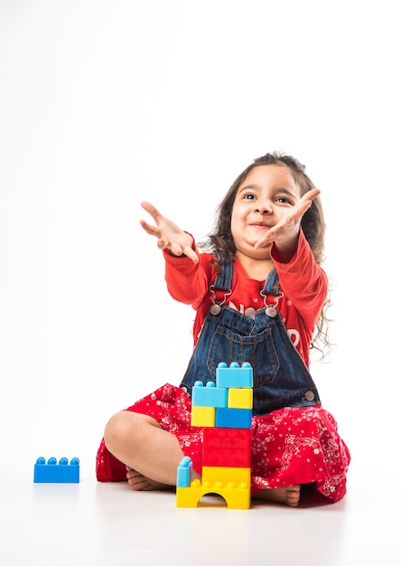 白い背景の上のカラフルなブロックのおもちゃで遊ぶかわいい小さなインドのアジアの女の子