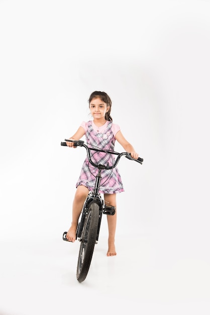 Cute little Indian or asian girl riding on bicycle, isolated over white background holding balloons