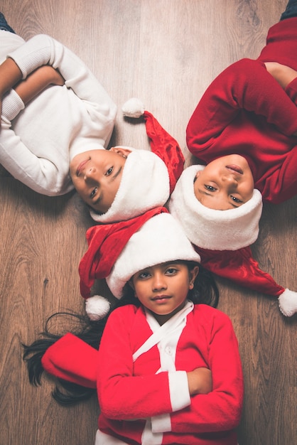 Cute little Indian Asian kids celebrating Christmas at home with Santa Hat, Gifts and Xmas Tree