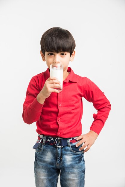 Cute little Indian or Asian playful boy holding or drinking a glass full of Milk, isolated over  white background