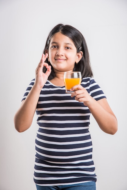 흰색 배경 위에 절연 유리에 신선한 망고 또는 오렌지 주스 또는 차가운 음료 또는 음료를 마시는 귀여운 인도 또는 아시아 장난 소녀