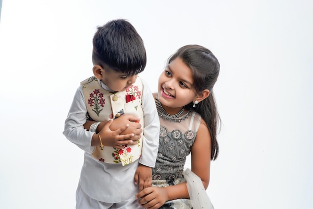 Cute little Indian asian siblings standing and embracing each other in white clothes ethnic standing against white background