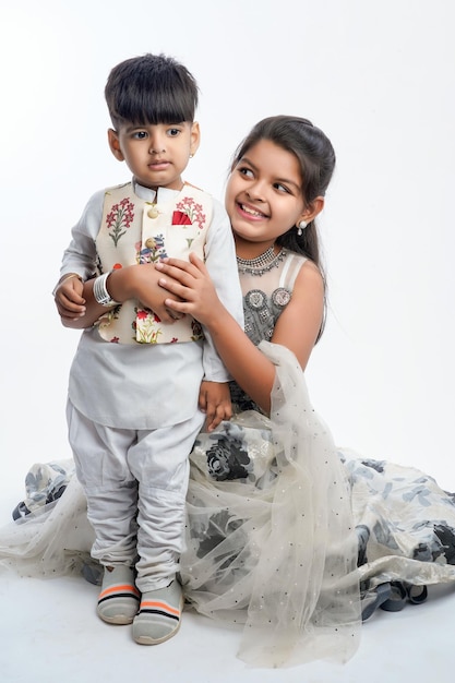 Cute little Indian asian siblings standing and embracing each other in white clothes ethnic standing against white background