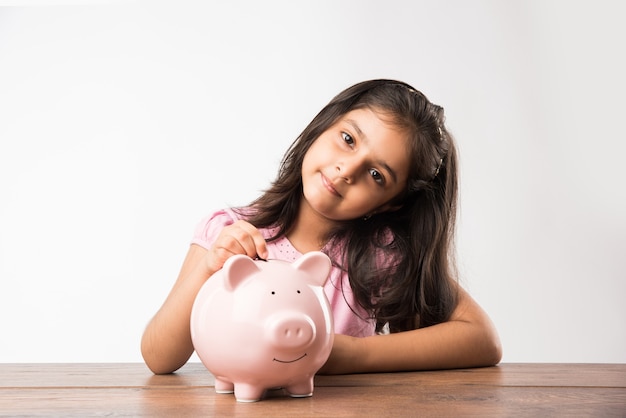 Cute little Indian or asian with Piggy Bank, putting coins, or thinking or showing thumbs up. Planning for future