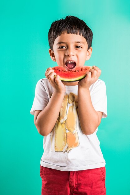 Cute little Indian boy eating watermelon slice, standing isolated over green background