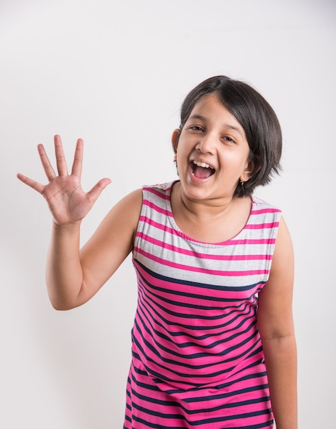 Милая маленькая индийская девочка считает число пальцем правой руки, изолированным на белом фоне