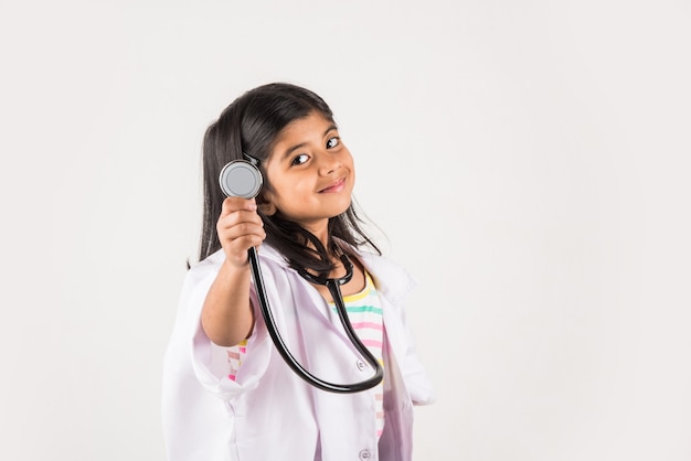 Cute Little Indian girl doctor with stethoscope while wearing Doctor's uniform. Standing isolated over white background