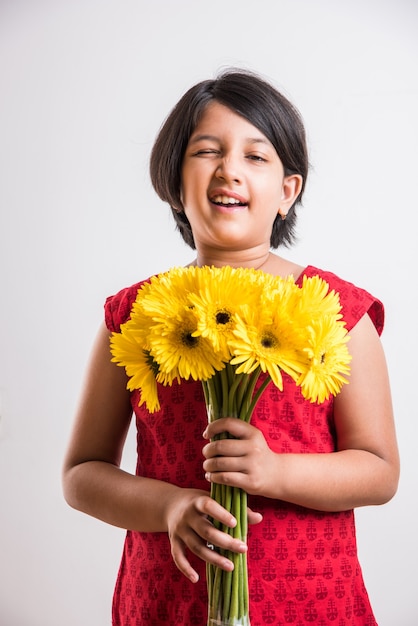 新鮮な黄色のガーベラの花の束または花束を保持しているかわいい小さなインドの女の子。白い背景の上に分離