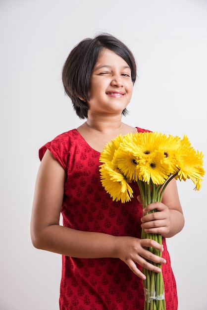 新鮮な黄色のガーベラの花の束または花束を保持しているかわいい小さなインドの女の子。白い背景の上に分離