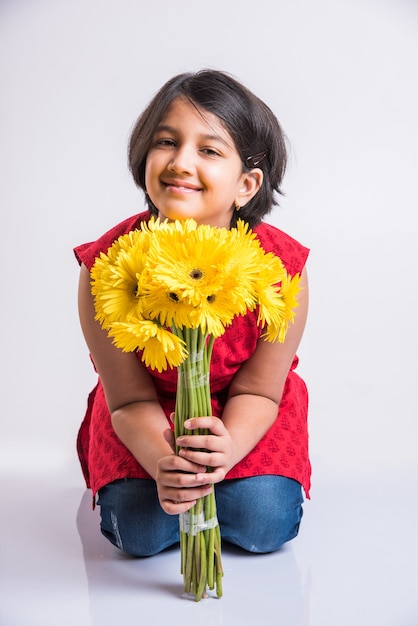 新鮮な黄色のガーベラの花の束または花束を保持しているかわいい小さなインドの女の子。白い背景の上に分離