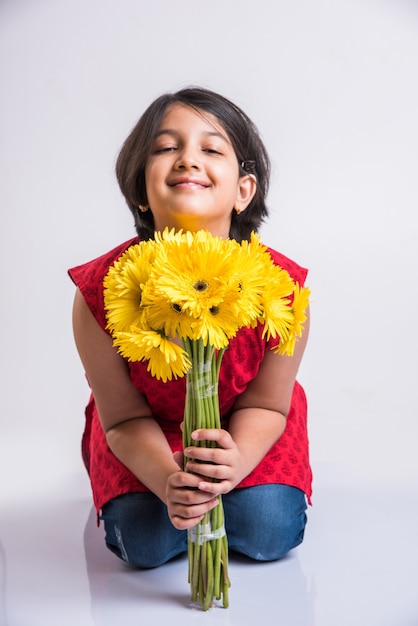 新鮮な黄色のガーベラの花の束または花束を保持しているかわいい小さなインドの女の子。白い背景の上に分離