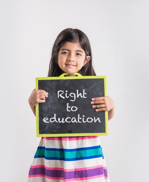 Cute little indian girl showing blank or abc written on black school slate board, isolated over white background