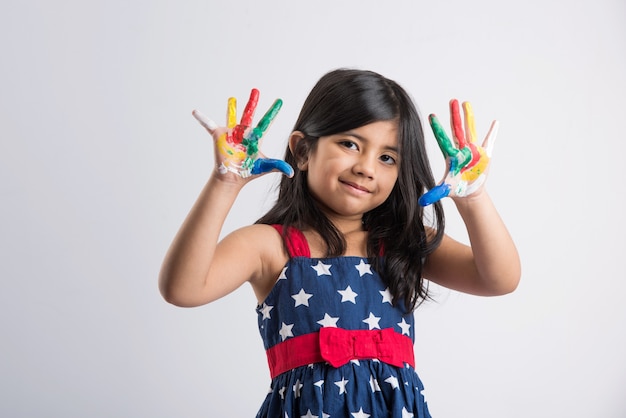 Cute little Indian girl showing her colourful hands or palm printing or painting or playing holi festival with colours, isolated over white background