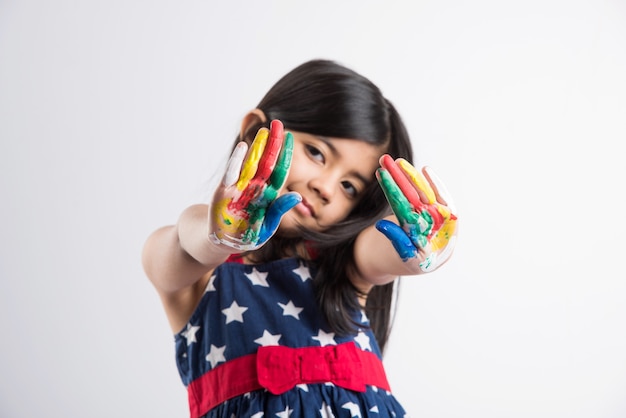 Cute little Indian girl showing her colourful hands or palm printing or painting or playing holi festival with colours, isolated over white background