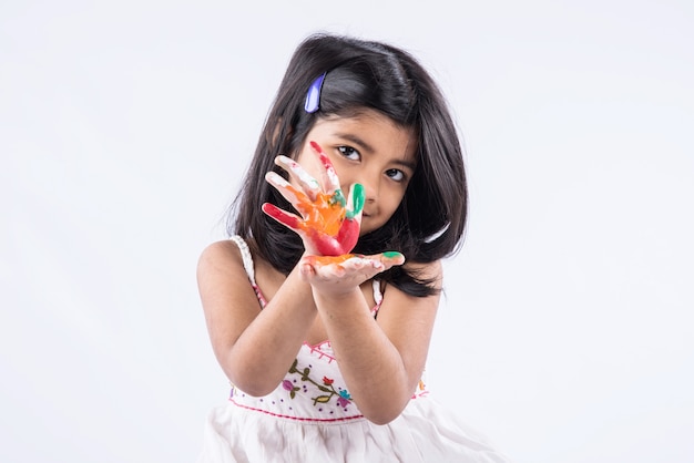 Cute little Indian girl showing her colourful hands or palm printing or playing holi festival with colours, isolated over white background