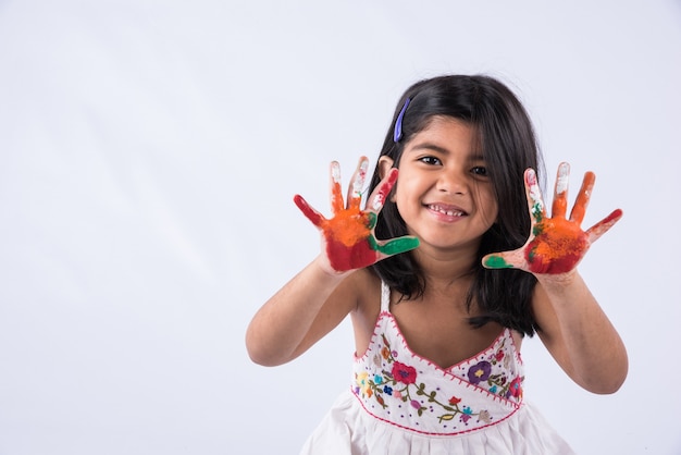 Carina bambina indiana che mostra le sue mani colorate o la stampa del palmo o gioca al festival di holi con i colori, isolato su sfondo bianco