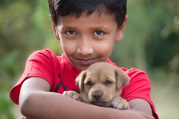 子犬の犬を抱き、カメラを探しているかわいい小さな無邪気な少年