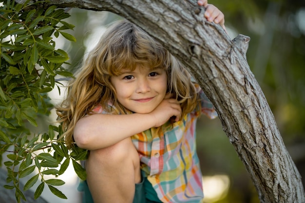 Cute little kid boy enjoying climbing on tree on summer day Cute child learning to climb having fun in summer park Happy kids time in nature Funny kids face