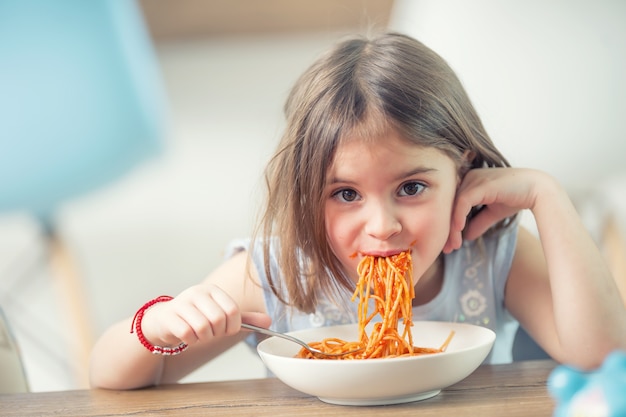 Cute little kid girl eating spaghetti bolognese at home.