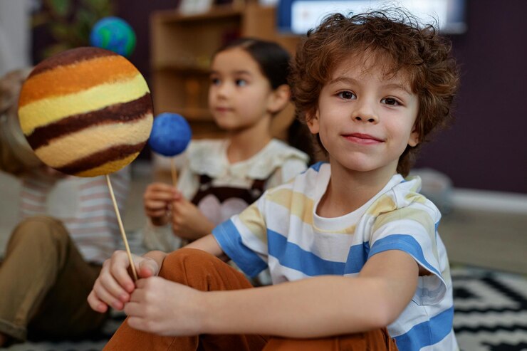 Photo cute little kid holding planet model and smiling at camera in preschool class