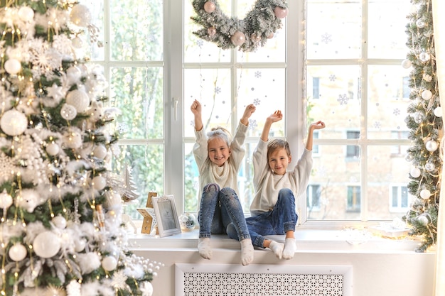 Cute little kids, boy and girl sitting on window sill