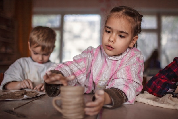 Cute little kids playing together with modeling clay in pottery workshop, craft and clay art