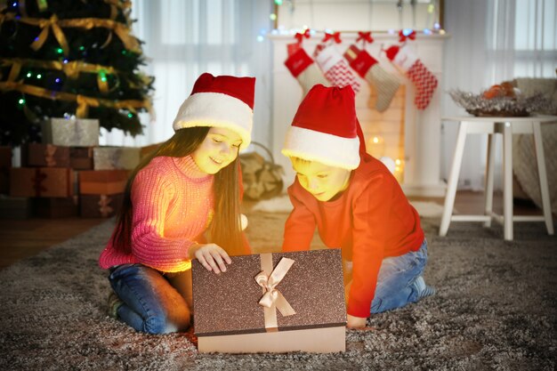 自宅でクリスマス プレゼントとサンタ帽子のかわいい子供たち