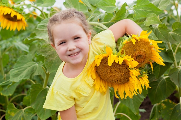 A cute little laughing girl in a field of sunflowers is holding a bouquet of flowers