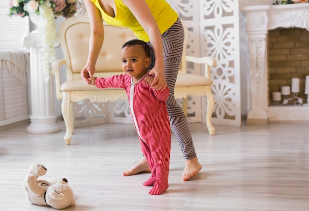 Photo cute little mixed race baby learning to walk, mom is holding his hands