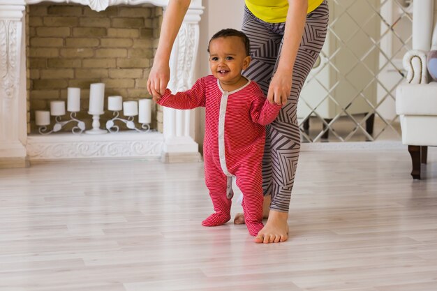 Simpatico bambino di razza mista che impara a camminare, la mamma gli tiene le mani