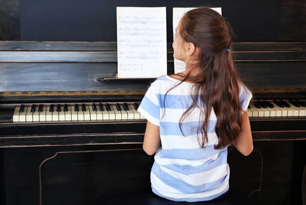 Cute little musician girl plays piano back view