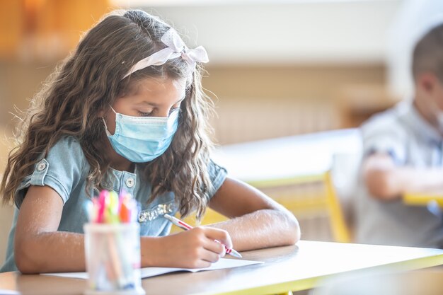 Cute little pupil girl with face mask back at school during COVID-19 quarantine.