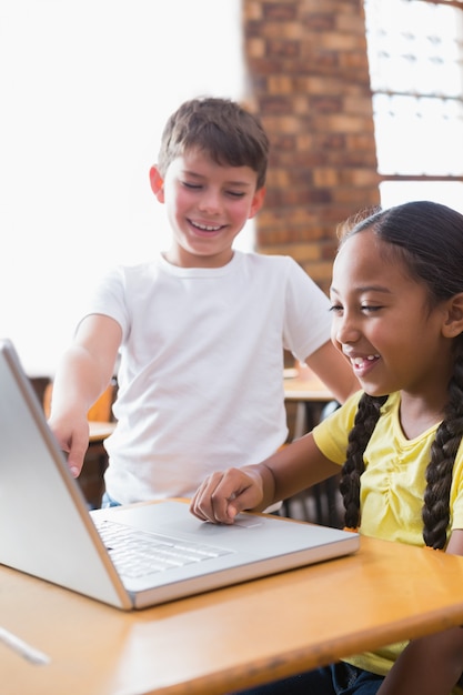 Cute little pupils looking at laptop in classroom