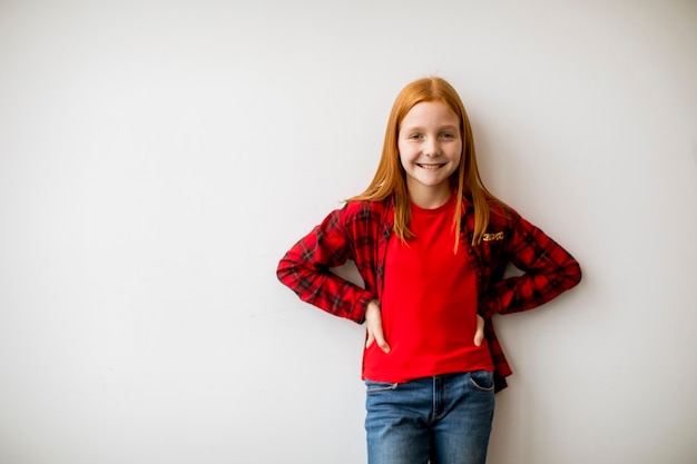 Bambina sveglia dei capelli rossi che fa una pausa il muro bianco