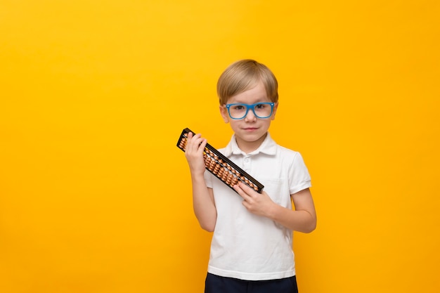 Cute little school boy in glasses holding abacus on yellow