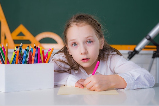 Cute little schoolboy drawing an house and looking at camera