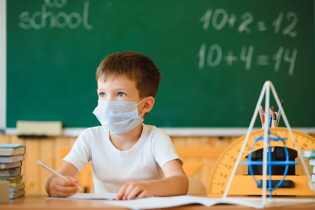 Cute little schoolboy sitting in the classroom with a mask