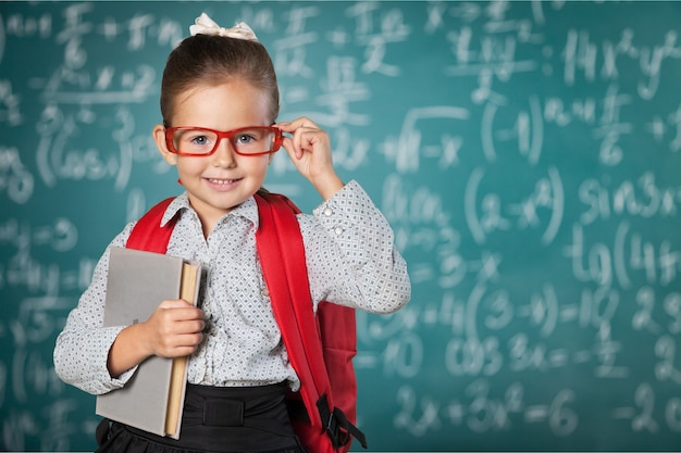 Cute little schoolgirl in glasses on blackboard background